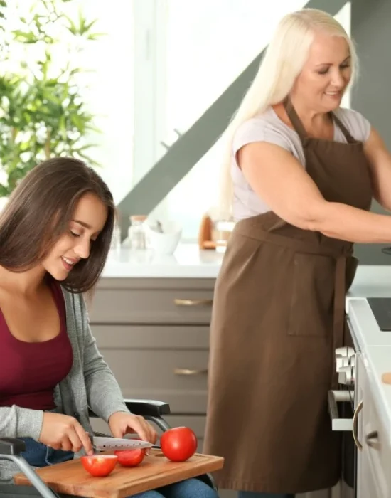 Woman in wheelchair cutting vegetables with assistance from carer